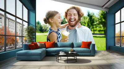 Laughing girl with ice-cream and her father having fun in park at leisure Wall mural