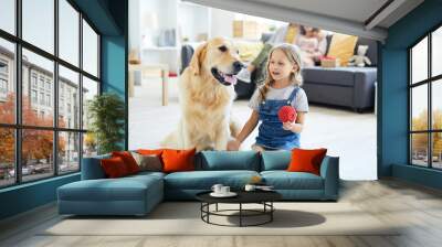 Little girl holding red rubber toy while sitting next to labrador pet and playing with him Wall mural