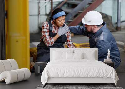 mature foreman in workwear giving first aid to female subordinate with pain in her shoulder after ac Wall mural