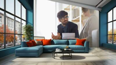 Modern middle eastern man wearing creative haircut and glasses listening intently to his colleague during  discussion of business ideas in modern office Wall mural