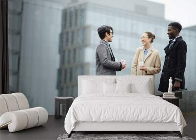 Multi-ethnic group of smiling business people meeting in snowy city street, smiling and talking, holding coffee cups against background of modern buildings Wall mural