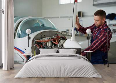 Portrait of modern aircraft engineer repairing jet plane in hangar, disassembling engine and fixing propeller motors Wall mural