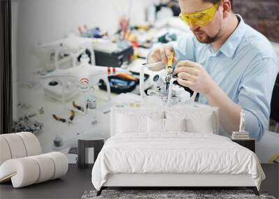 Portrait of modern man setting up new high tech drones and attaching cameras in electronic workshop Wall mural