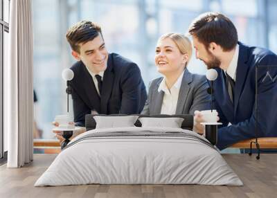 Portrait of three business people, one woman and two men, smiling cheerfully while chatting in glass hall of modern office building leaning on railing and holding coffee cups Wall mural