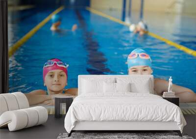 Portrait of two schoolgirls smiling and looking at camera at pool swimming practice Wall mural