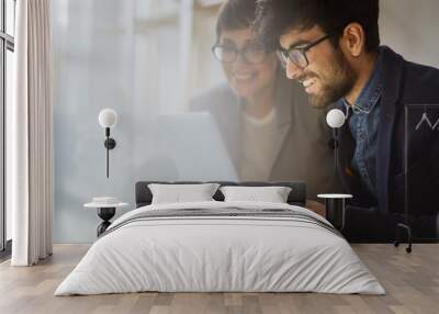 Portrait of two successful businesspeople checking statistics information, both smiling joyfully while looking at laptop screen Wall mural