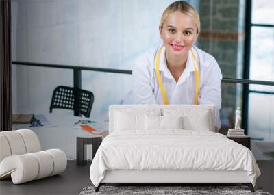 Pretty young blonde fashion designer looking at you during work in studio Wall mural