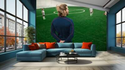 Rear view of football trainer in activewear standing on field and watching for players Wall mural