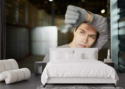 Restful pensive young guy working at distribution warehouse leaning on cargo container and looking into distance Wall mural