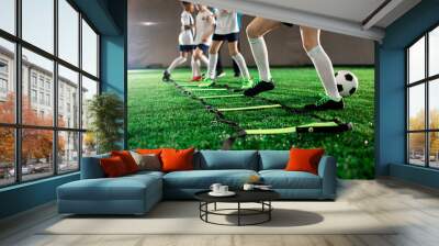 Row of little football players keeping their legs over square cells on green field during training Wall mural