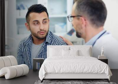 Sad young man listening to his doctor encourage after voicing diagnosis Wall mural