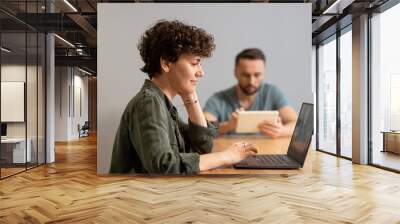 Side view of young businesswoman sitting in front of laptop against her husband Wall mural