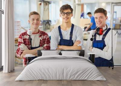 Smiling confident young carpentry students in blue uniform standing in line and looming at camera in workshop Wall mural