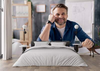 Smiling mature engineer sitting by table while working over new sketches Wall mural