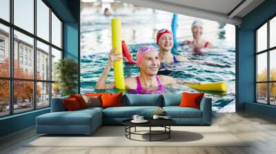 smiling mature female in swimwear and two more active women listening to trainer advice during gymna Wall mural