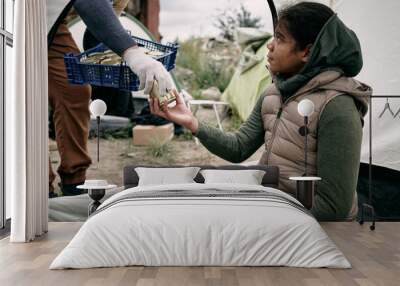 Social worker with box of preserves giving canned food To thankful middle-eastern refugee girl living in tent after escape Wall mural