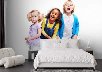 Studio portrait of children against white background:  full body shot of three kids in colorful clothes, African girl, blond boy and cute little girl, laughing and screaming loudly with mouths open Wall mural