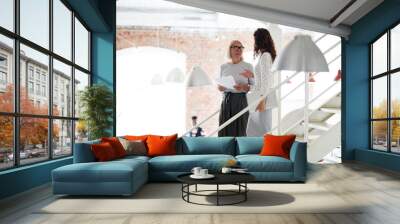 Two businesswomen going down the stairs of modern office and communicating with each other Wall mural