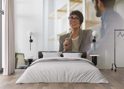 two cheerful colleagues smiling while discussing something in modern office, focus on stylish busine Wall mural