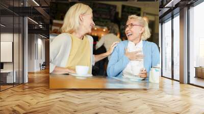 Two female friends laughing during their talk by cup of tea while relaxing in cafe at leisure Wall mural