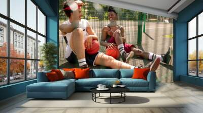 Two intercultural guys in activewear having rest on basketball court Wall mural