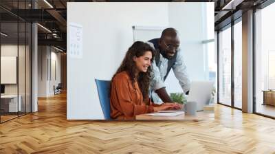 Two young creative designers working over new project in front of laptop while smiling businesswoman entering points and ideas Wall mural