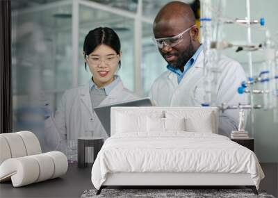 Two young intercultural chemists looking at screen of tablet held by African American male scientist while carrying out new trial Wall mural