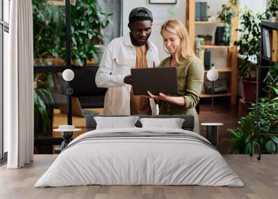 Two young intercultural employees in casualwear looking at screen of laptop held by blond businesswoman during discussion Wall mural