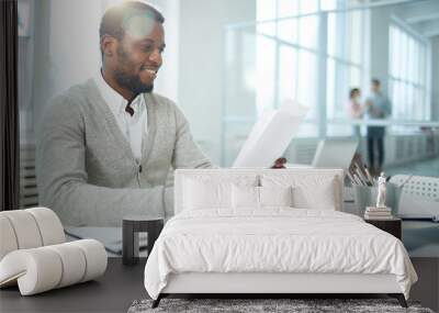 Waist-up portrait of cheerful African American businessman studying document while sitting at desk of modern open plan office, lens flare Wall mural