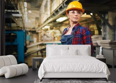 Waist-up portrait of pretty young engineer looking away while working on digital tablet,  interior of manufacturing plant on background Wall mural