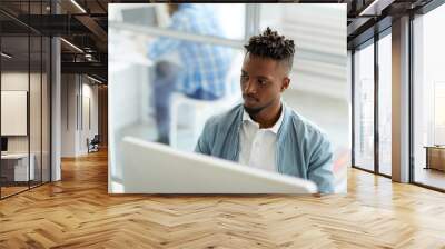 Young African-american businessman sitting in front of two computer monitors and analyzing data Wall mural