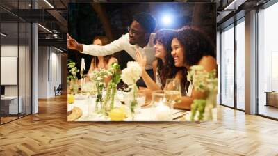 Young black man taking selfie with happy intercultural lesbian brides boasting with their wedding rings by served festive table Wall mural