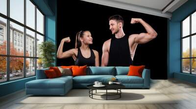 Young cheerful sports couple in activewear looking at each other while showing their strength in front of camera Wall mural