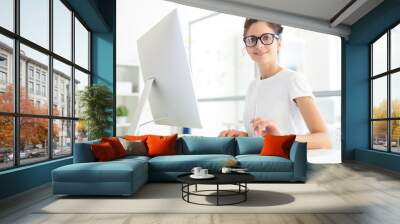 Young confident manager or designer sitting by her workplace in office in front of computer monitor Wall mural