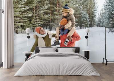 Young contemporary family of father, mother and son enjoying winter day in park while African American man carrying little boy on shoulders Wall mural