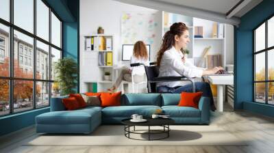 Young disable office worker in wheelchair sitting by desk in front of laptop and networking Wall mural