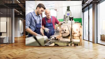 Young engineer looking at rotating detail of industrial machine while his senior colleague explaining how it works Wall mural