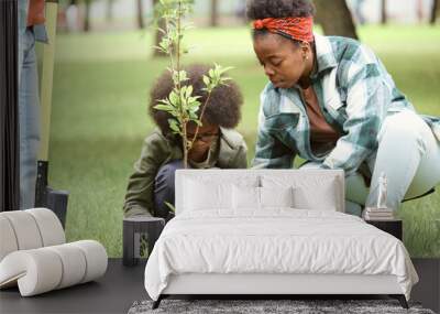 Young female and her little son planting tree in one of city parks on summer day Wall mural