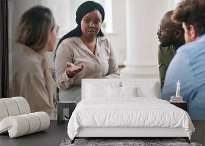 Young female psychotherapist giving advice to one of patients during session while sitting in front of group of people with problems Wall mural