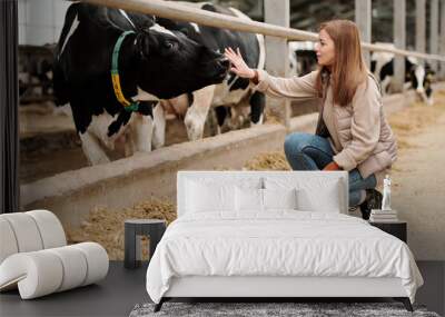 Young female worker of large animal farm sitting on squats by paddock with cows Wall mural