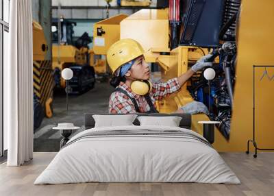 Young Hispanic female in protective helmet, coveralls and gloves checking engine of huge industrial machine before repairing Wall mural