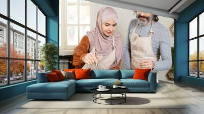 Young Muslim female trainee in hijab holding whisker over metallic pan on stove Wall mural