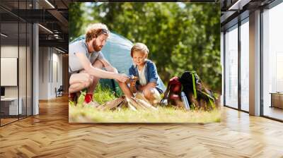 Young scout showing his son how to make campfire during trip in natural environment Wall mural