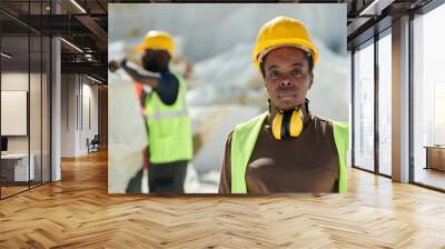 Young serious African American female worker of marble quarry in uniform and protective helmet looking at camera outdoors Wall mural