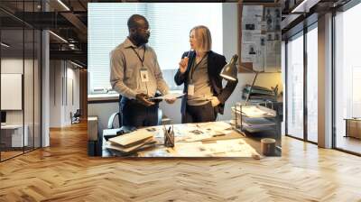 Young serious African American male FBI agent listening to mature female colleague in formalwear with pen by her chin Wall mural