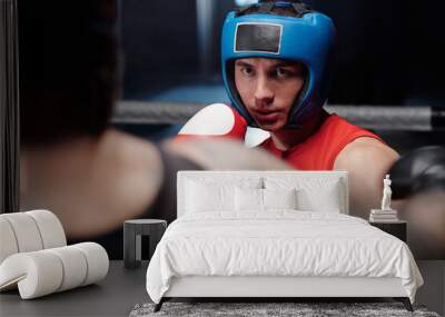 Young serious boxer in protective face shield looking at his rival attacking him and thinking over blow during sparring round on ring Wall mural