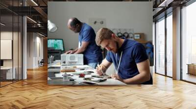 Young serious specialist of troubleshooting and repair service center with transmission tweezers bending over workplace with motherboard Wall mural