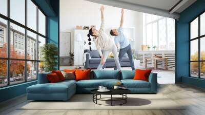 Young sporty couple in activewear raising their left arms while exercising in living-room at home Wall mural