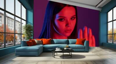 Young strict brunette looking at you and keeping hand in front of herself Wall mural