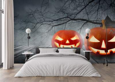 Two spooky Halloween pumpkins, Jack O Lantern, with an evil faces and eyes on a wooden table with a misty gray background. Wall mural